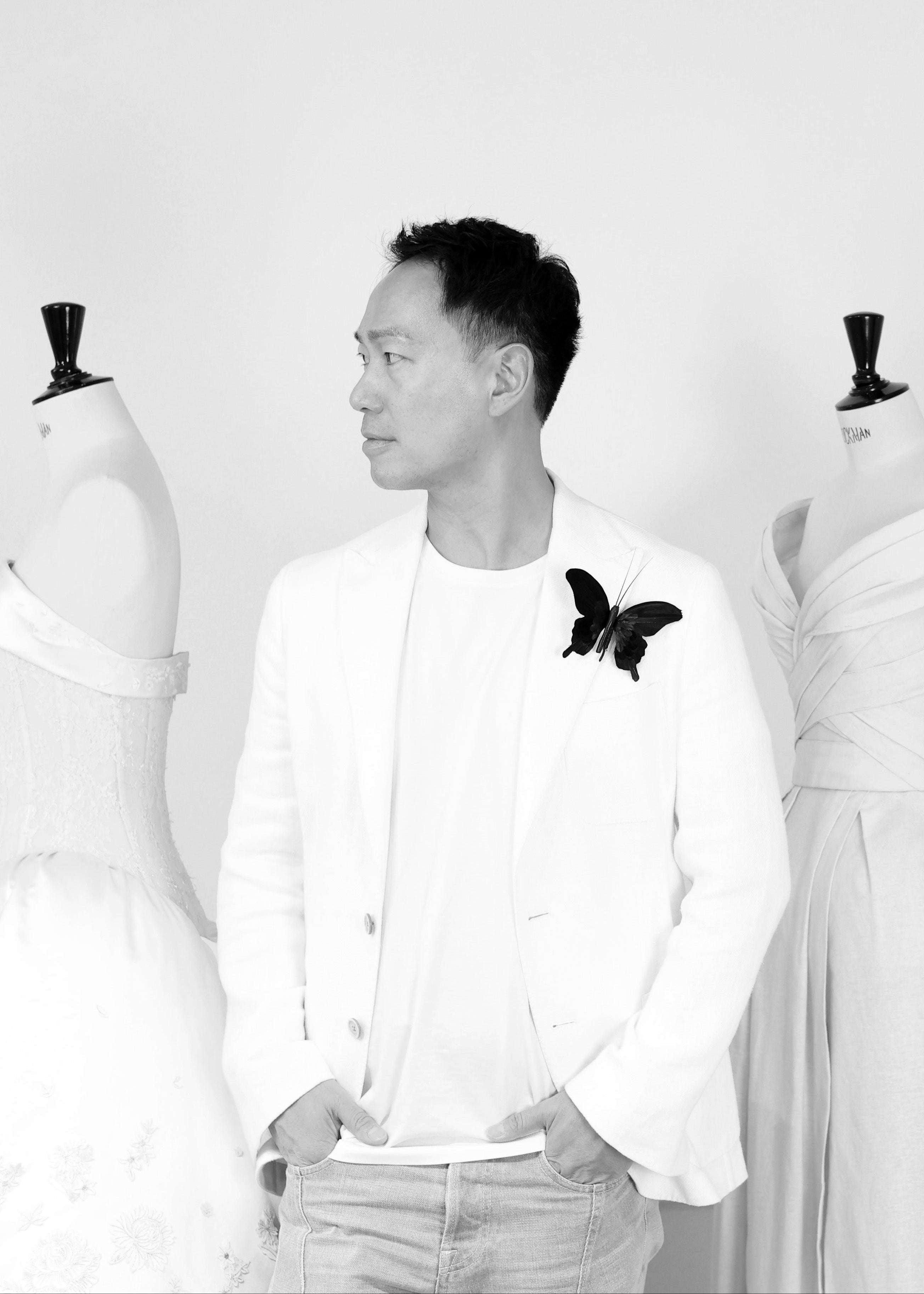 Budi wearing a white shirt with a butterfly pin in front of mannequins.